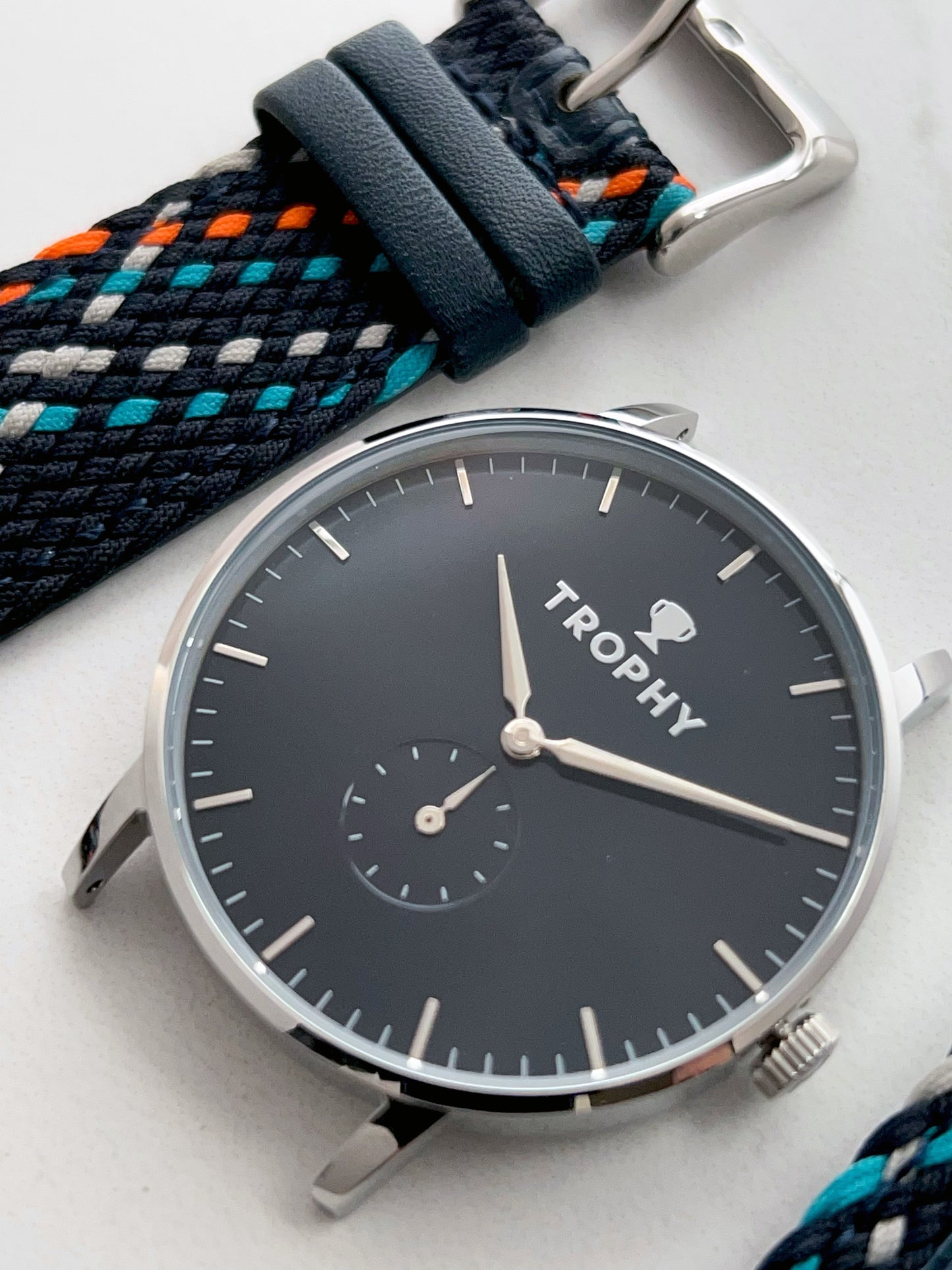 Trophy Watch Company | 40mm EMBERLINE PERLON: The Emerline Perlon brings an air of sporty sophisticaion to anyone who wears it. Truly unique in design and appearance, this watch makes a strong statement. The perlon strap has cords of navy blue, grey, teal